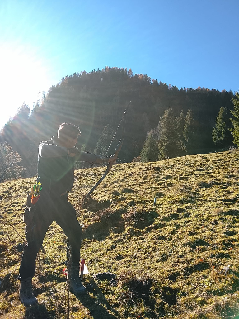 Bogenschütze zielt mit Langbogen auf sonniger Wiese